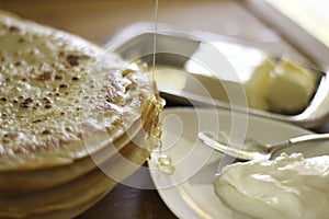 Maslenitsa. A stack of yeast pancakes drizzled with honey on a blurred background of butter and sour cream