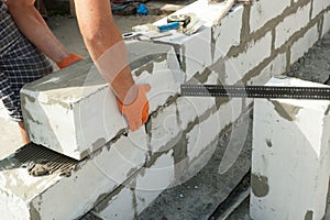 Mason aligning aerated autoclaved concrete block of constructed house wall.