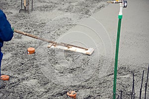 Mason building and leveling a first layer of fresh concrete floor at house foundation