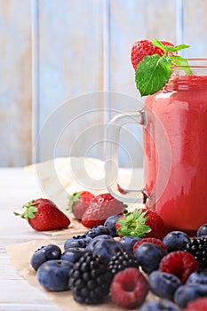 Mason jar of berry smoothie and fresh ingredients on white wooden table, closeup
