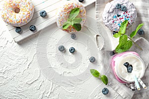 Mason jar with delicious blueberry milkshake and doughnuts on light table