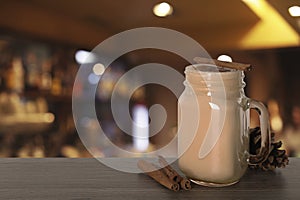 Mason jar with delicious eggnog, cinnamon sticks and cone on wooden table in bar, space for text