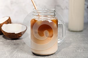 Mason jar of delicious iced coffee with coconut syrup on light grey table, closeup