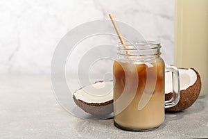 Mason jar of delicious iced coffee with coconut syrup on light grey table. Space for text