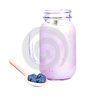 A mason jar full of yogurt with mixed berries, isolated on a white background. Healthful blueberries in a wooden spoon.