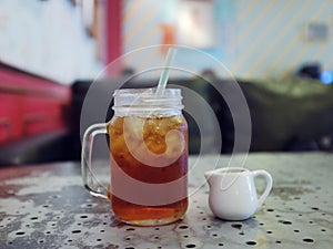 Mason jar glass of iced tea with straw and milk jug