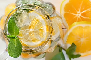 Mason jar of a homemade lemonade with mint and ice, citrus slices on a rustic white wooden background