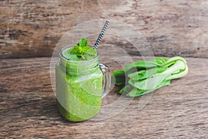 Mason jar mugs filled with green spinach, banana and coconut milk health smoothie with with a spoon of oatmeal on wooden rustic ta
