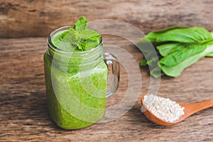 Mason jar mugs filled with green spinach, banana and coconut milk health smoothie with with a spoon of oatmeal on wooden rustic ta