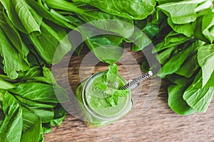 Mason jar mugs filled with green spinach, banana and coconut milk health smoothie with with a spoon of oatmeal on wooden rustic ta