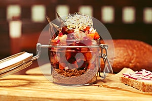 Mason jar with pieces of vegetables carrot, onion, capers, red beet, anchovy, brown bread crumbles and seedlings of lucerne