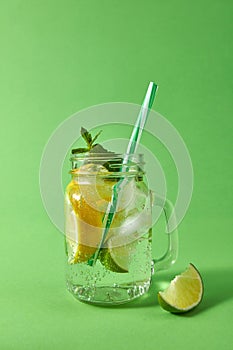 Mason jar with sparkling ackoholic mojito with ice, slices of lime and lemon, leaf of mint with colored plastic straws