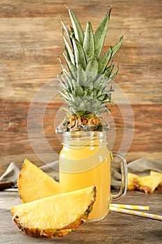 Mason jar of sweet juice with pineapple slices on wooden table