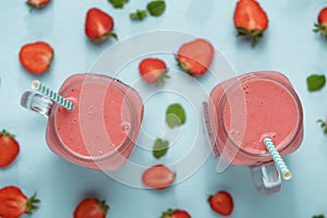 Mason jars with strawberry smoothie of milkshake on blue table with berries halfs.