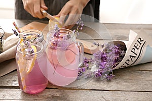 Mason jars with tasty beverage and young woman preparing lavender lemonade at table