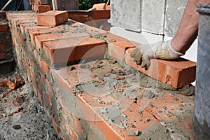 Mason is laying bricks applying mortar to build a brick wall of the house construction