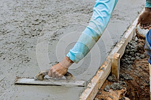 Mason worker is holding steel trowel and smoothing plastering new sidewalk on wet freshly poured concrete
