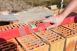Mason worker measuring with professional level the new bricks wall under construction