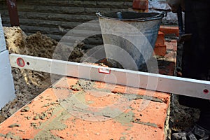 Masonry construction tools. A close-up of a spirit level and a bucket with mortar on a brick wall, brick foundation of a new house