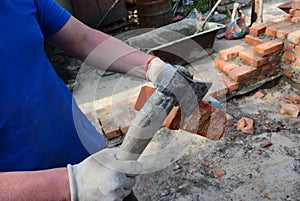 Masonry. How to hand cut a brick. A bricklayer is cutting a brick using a masonry tool, an axe while a brick wall, foundation