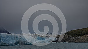 A mass of blue cracked ice between the mountain slopes. Breakaway icebergs float in a turquoise glacial lake. Fog. Perito Moreno g