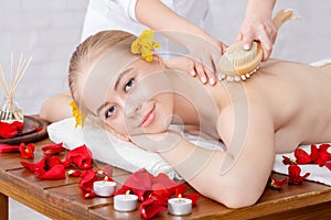 Massage with brush. Smiling girl receives massage on massage table with rose petals