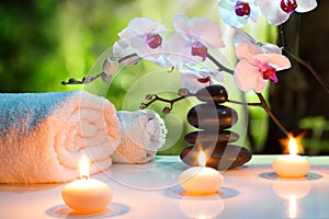 Massage composition spa with candles, orchids and black stones in garden