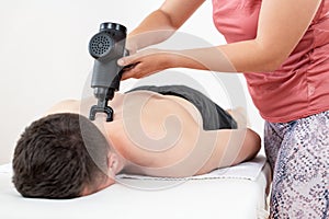 Massage gun background. Young female physiotherapist using handheld massaging gun to relieve neck muscle pain. photo