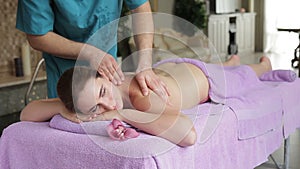 In massage room woman lies on lilac towels and receives back massage.