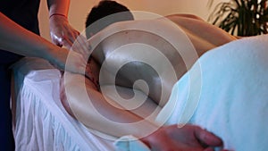Massage session in the spa centre in warm lighting - woman doctor massaging her client`s shoulder - half of his body