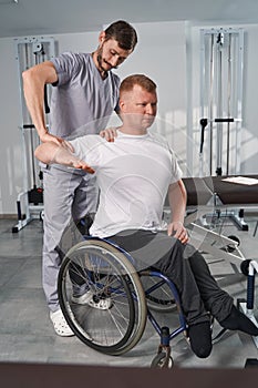 Massage therapist checks hand joint flexibility of man with paraplegia