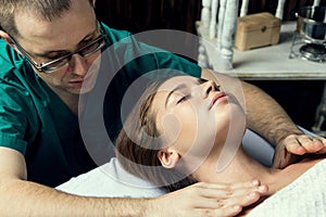 Massage therapist doing massotherapy of a young woman. Beautiful relaxed face of a young woman 26 years old with brown hair