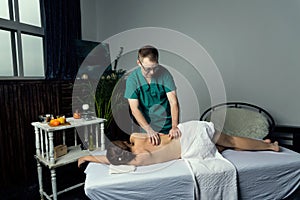 Massage therapist doing massotherapy of a young woman. Beautiful relaxed face of a young woman with brown hair and closed eyes