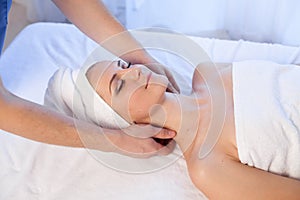 A massage therapist makes a woman face and neck massage in the Spa