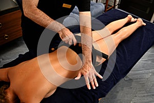 A massage therapist making a body massage to a young woman using a bamboo stick. Ayurvedic body care at the spa