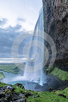 Masses of water cascade from the Seljalandsfoss waterfall down into a big lake.