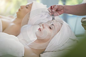 Masseur doing cream mask on face of beautiful young woman relaxing in the spa salon.