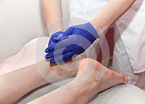 Masseur hands in blue protective gloves touch feet of woman patient doing foot massage procedure in spa salon.