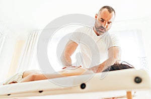 Masseur man doing massage manipulations on the client back and communicate with patient