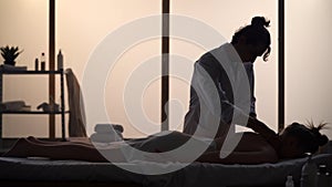 Masseur, massage specialist giving neck massage to his patient. Silhouettes of a woman and a man in the massaging room