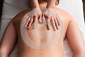 masseur massaging back and shoulder blades of young woman on massage table. Concept of massage spa treatments. Close-up
