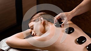 Masseur placed hot stone on the back of woman. Manual therapy in spa.