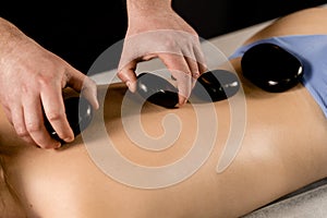 Masseur placed hot stone on the back of woman. Manual therapy in spa.