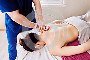 Masseur placed one palm on top of other, massaging woman back in shoulder area.