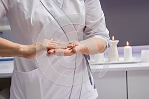 Masseur putting aroma oil on her hands, preparing for massage in spa center