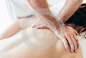 Masseur`s man hands doing massage manipulations on the Scapula area zone during young female body massaging