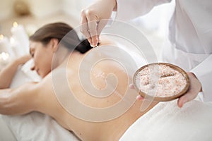 Masseuse applying mineral salt body scrub on back of young woman