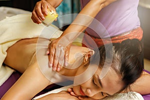Masseuse drips warm massage oil from a candle on the back of the young woman