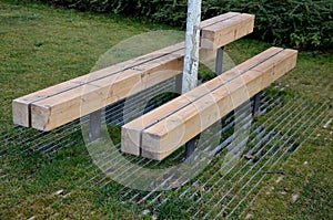 Massive bench in the park under a tree in the park urban style beam shape on metal legs in the square. grass grate made of metal a