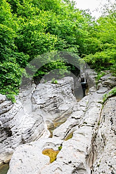 Massive chalk stones riverbed with wild river and pools formed by Okatse Waterfall in gorge of Satsikvilo, lush vegetation,